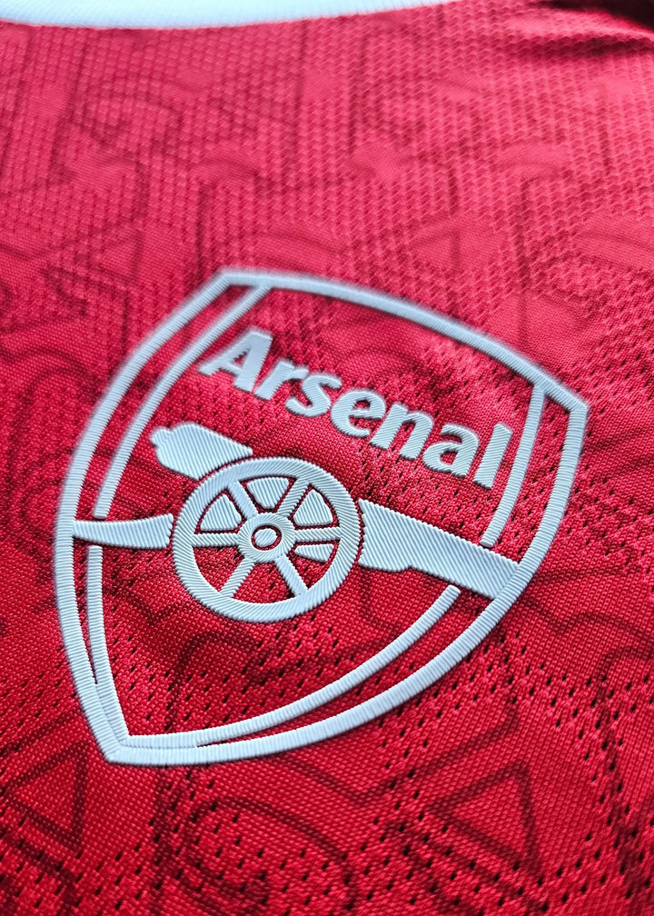 Close-up view of Arsenal crest with club name and cannon logo in white on a red background.