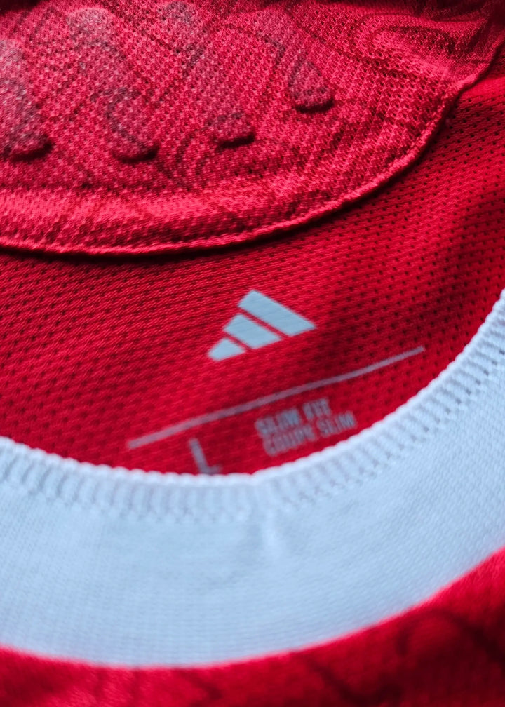 Close-up view of the adidas logo and care label on a red football shirt with a white collar.