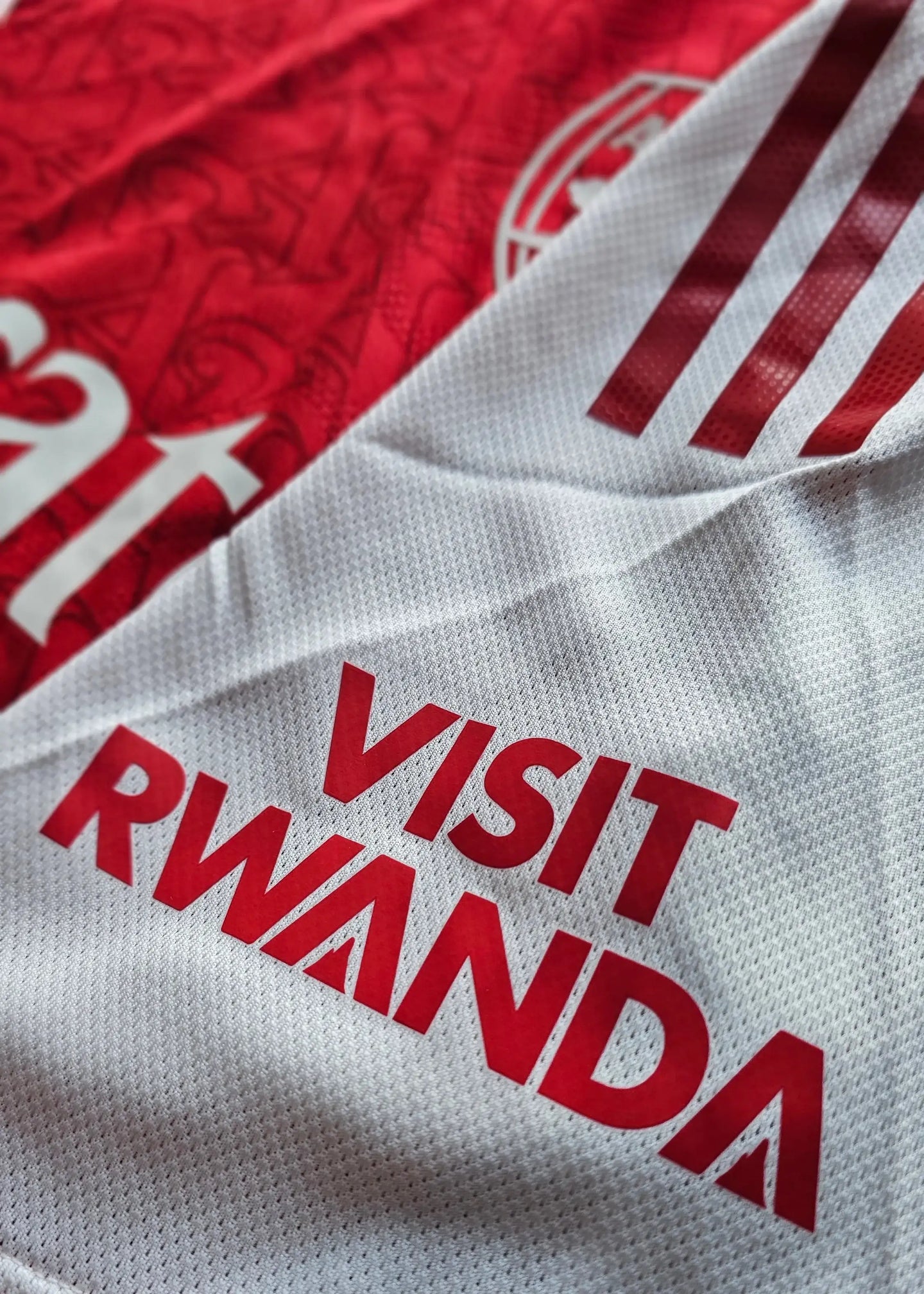 Detail showing white fabric with red 'VISIT RWANDA' text and Arsenal crest pattern.