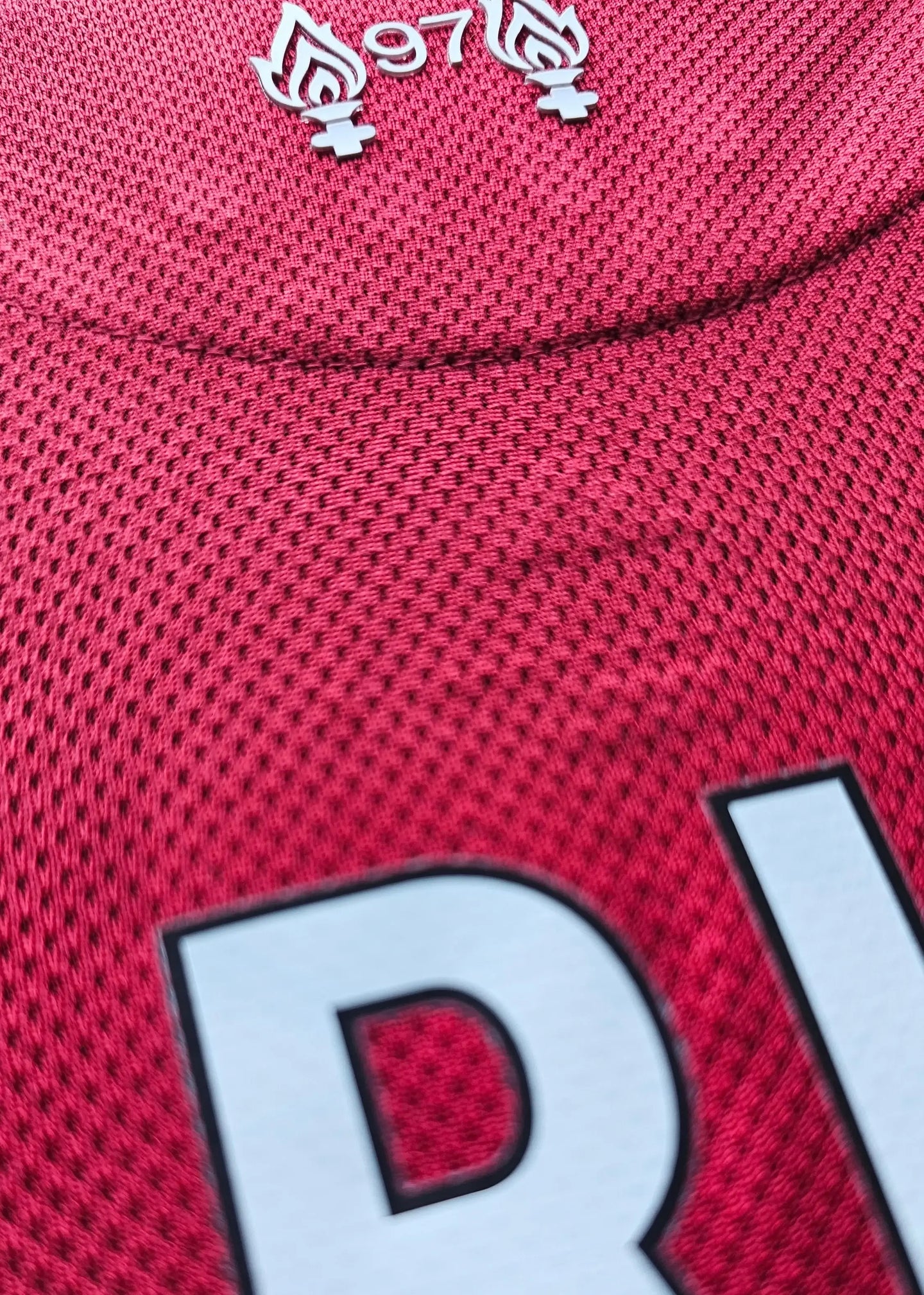 Detail showing the embroidered 97 flames symbol on a red Liverpool football shirt.
