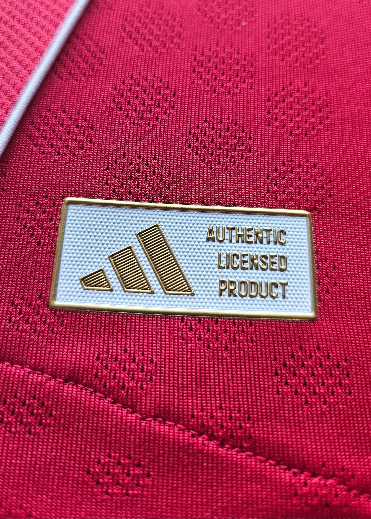 Close-up of the adidas label stating AUTHENTIC LICENSED PRODUCT on a red football shirt.