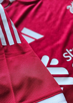 Close-up detail of the red football shirt showcasing white stripes and Liverpool crest.