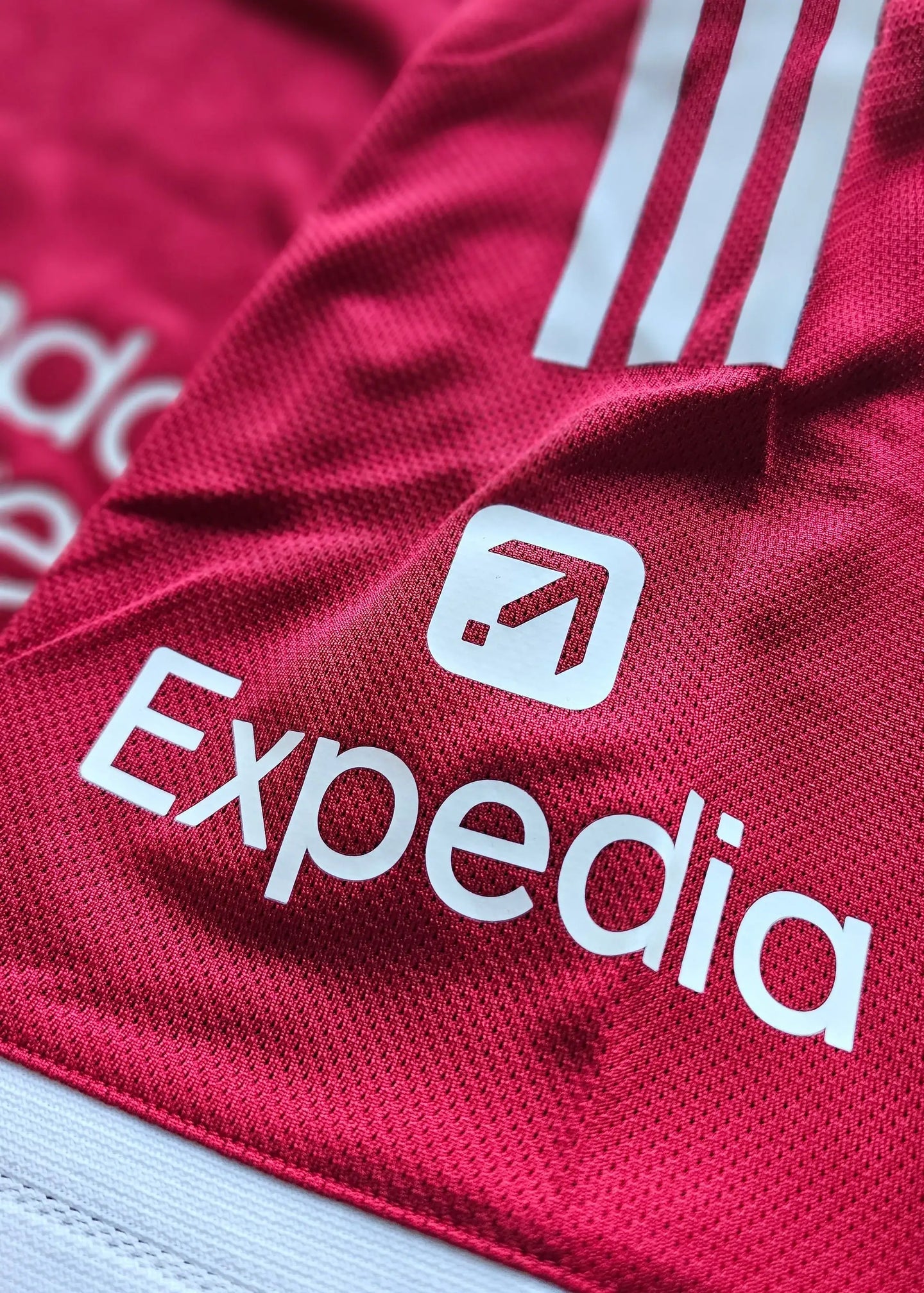 Close-up of the red football shirt featuring the Expedia logo and three white stripes.