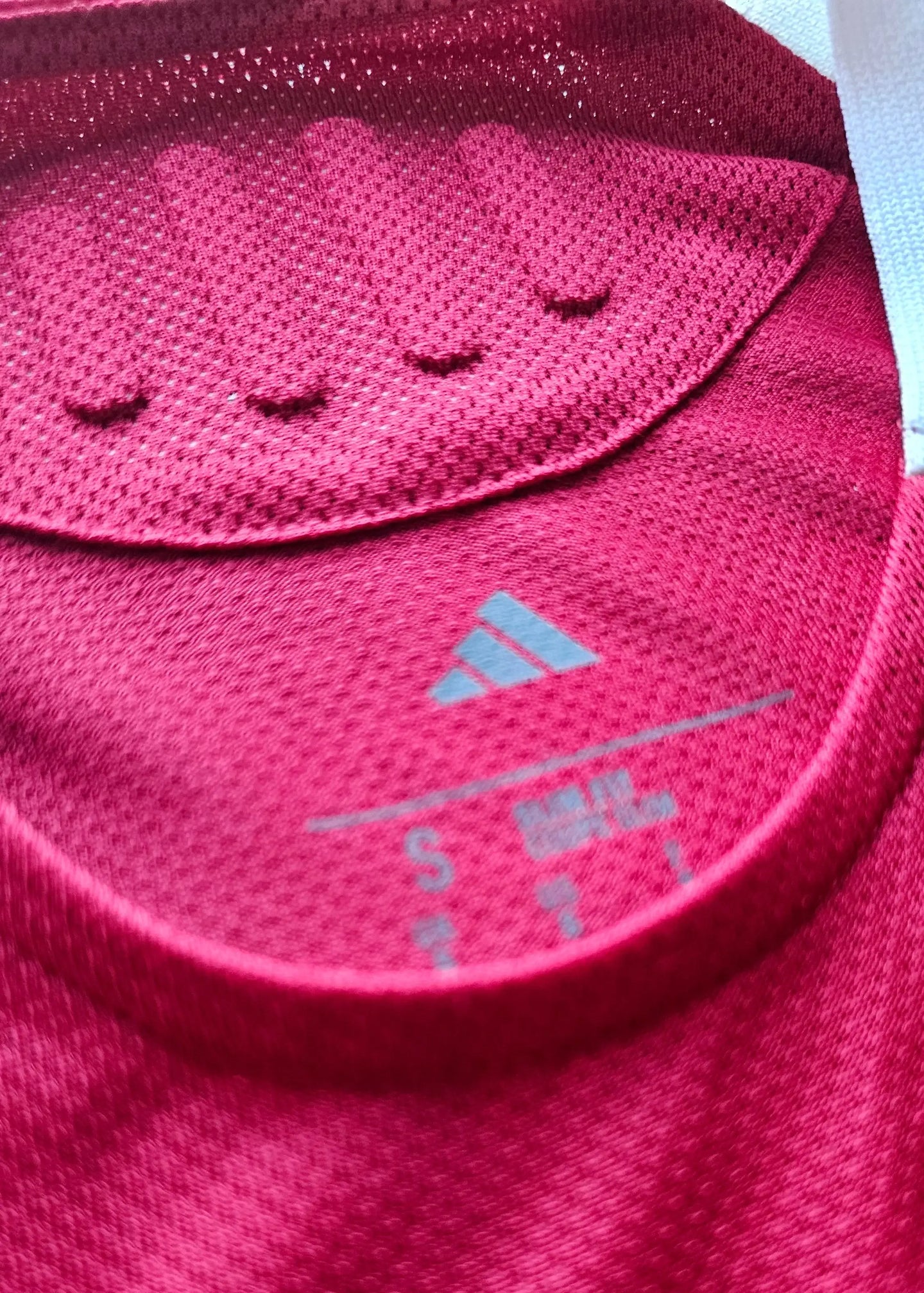 Close-up of adidas label showing size S on a red football shirt collar.