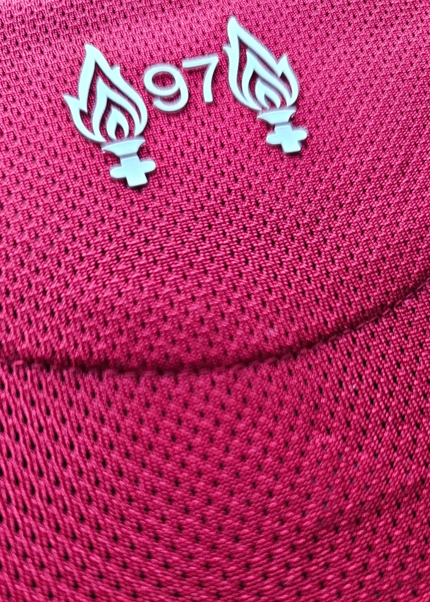 Close-up of Liverpool F.C. shirt displaying the '97' emblem with flames on a red textured background.