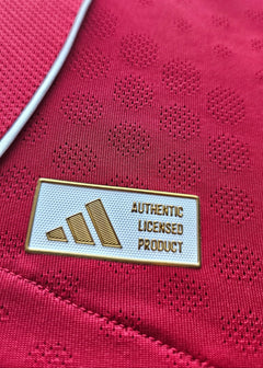 Detail of the "AUTHENTIC LICENSED PRODUCT" tag by adidas on a red football shirt.