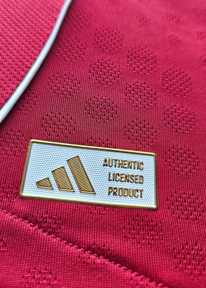 Detail of the "AUTHENTIC LICENSED PRODUCT" tag by adidas on a red football shirt.