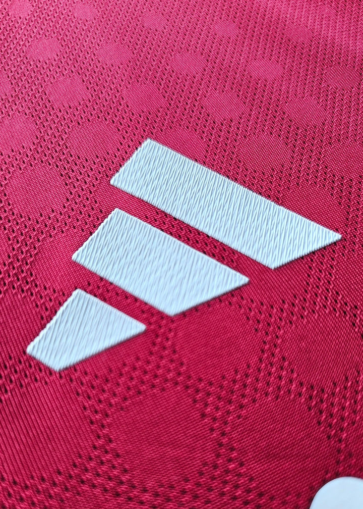 Close-up of white adidas three-stripe logo on red football shirt fabric with hexagonal texture.