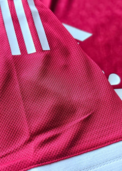 Close-up of vibrant red fabric featuring three white adidas stripes on a football shirt.