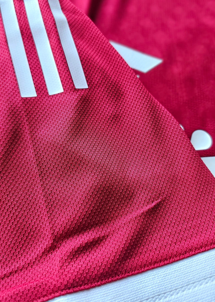 Close-up of vibrant red fabric featuring three white adidas stripes on a football shirt.