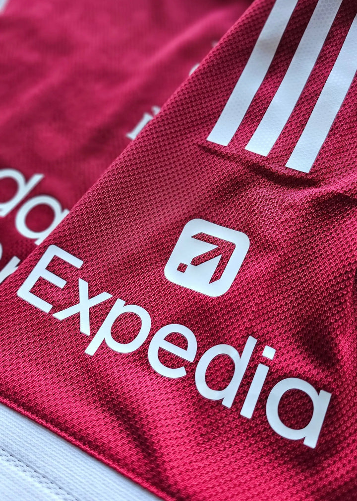 Detail view of red football shirt showing adidas logo and Expedia sponsor text.