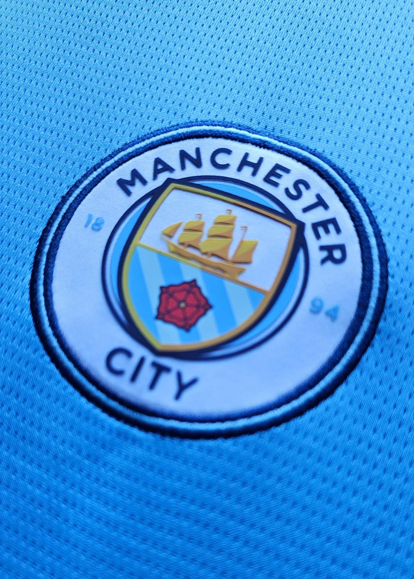Crest detail featuring the Manchester City logo with blue and yellow colors.