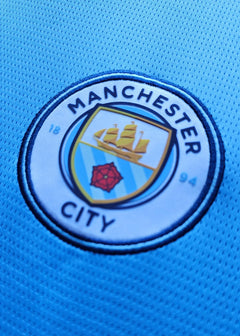 Crest detail featuring the Manchester City logo with blue and yellow colors.