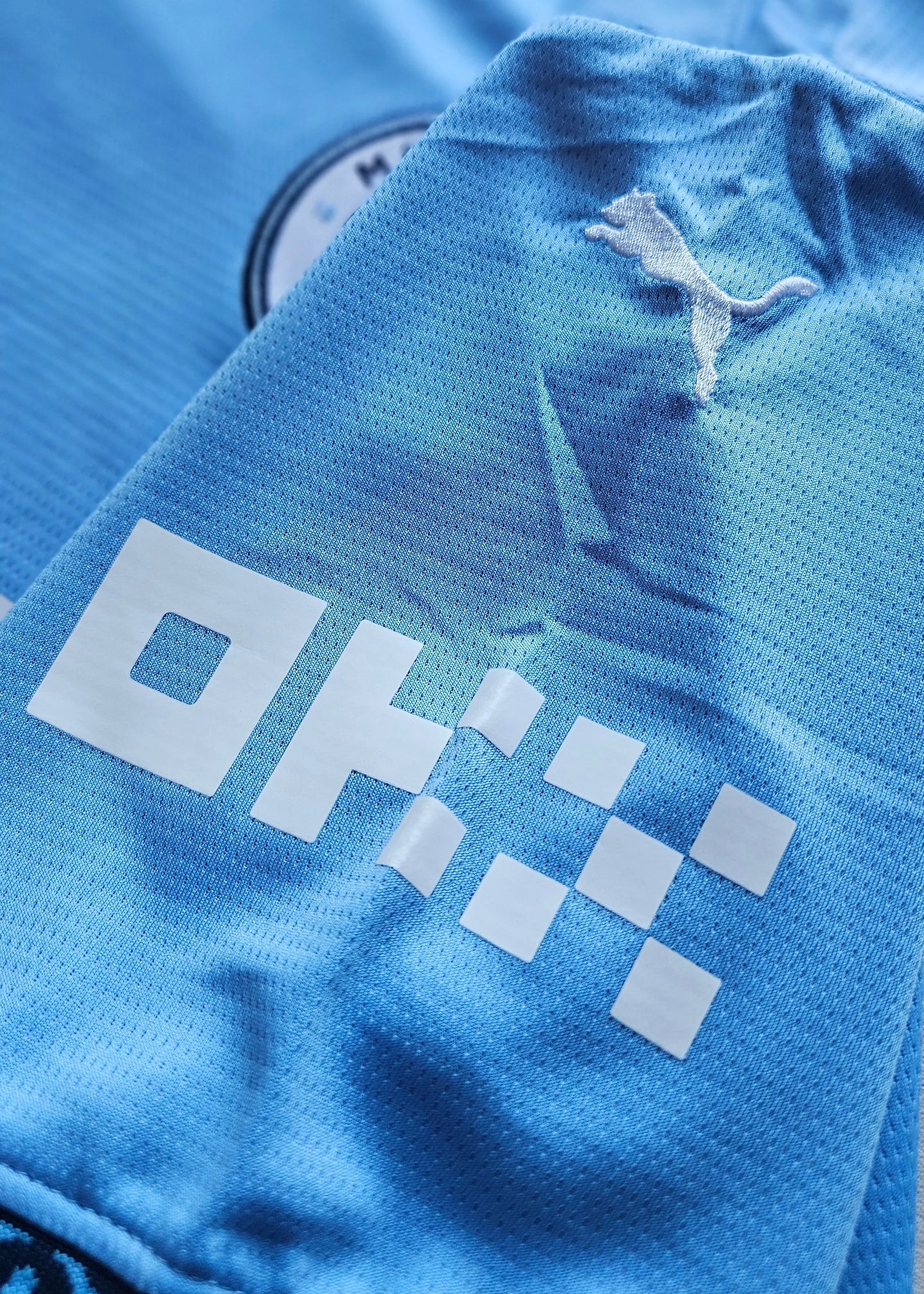 Close-up view showing the Puma logo and sponsor detail on a blue Manchester City football shirt.