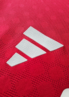 Close-up of white adidas logo on red football shirt fabric with textured pattern.