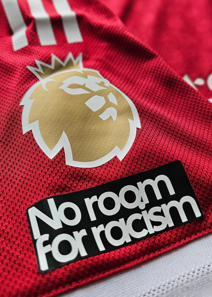Close-up of Liverpool crest and 'No room for racism' printed on a red football shirt.