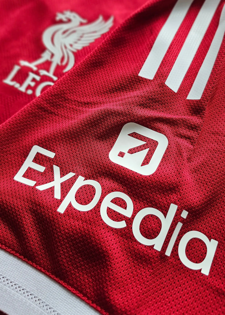 Close-up showing Liverpool F.C. crest and Expedia sponsor on red football shirt.