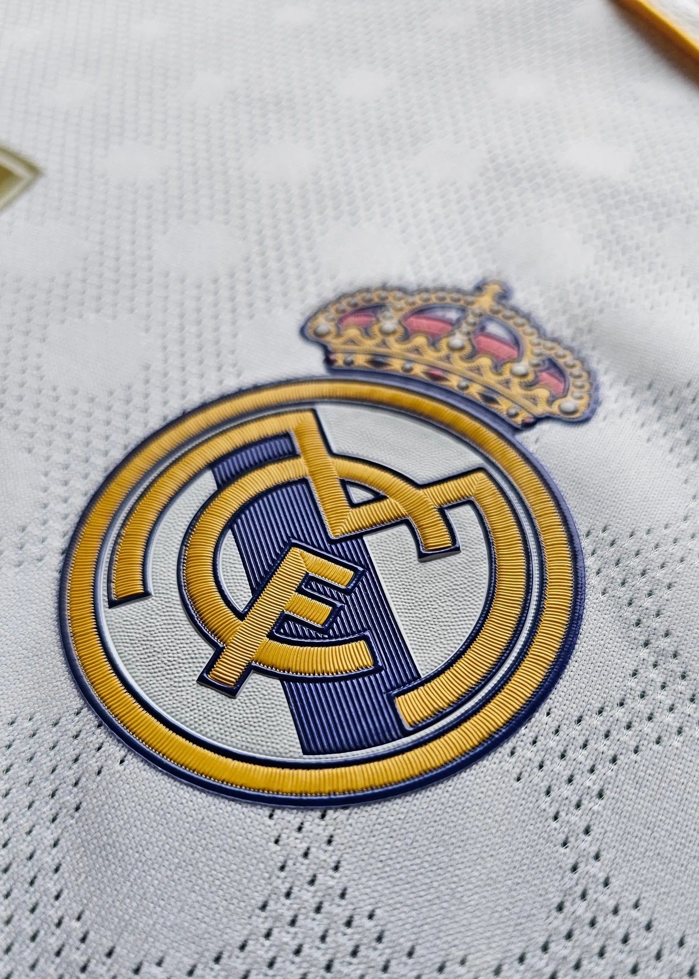 Crest detail of Real Madrid with gold crown and embroidered club logo on white fabric.