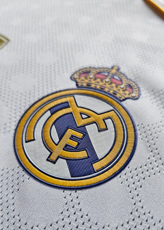 Crest detail of Real Madrid with gold crown and embroidered club logo on white fabric.