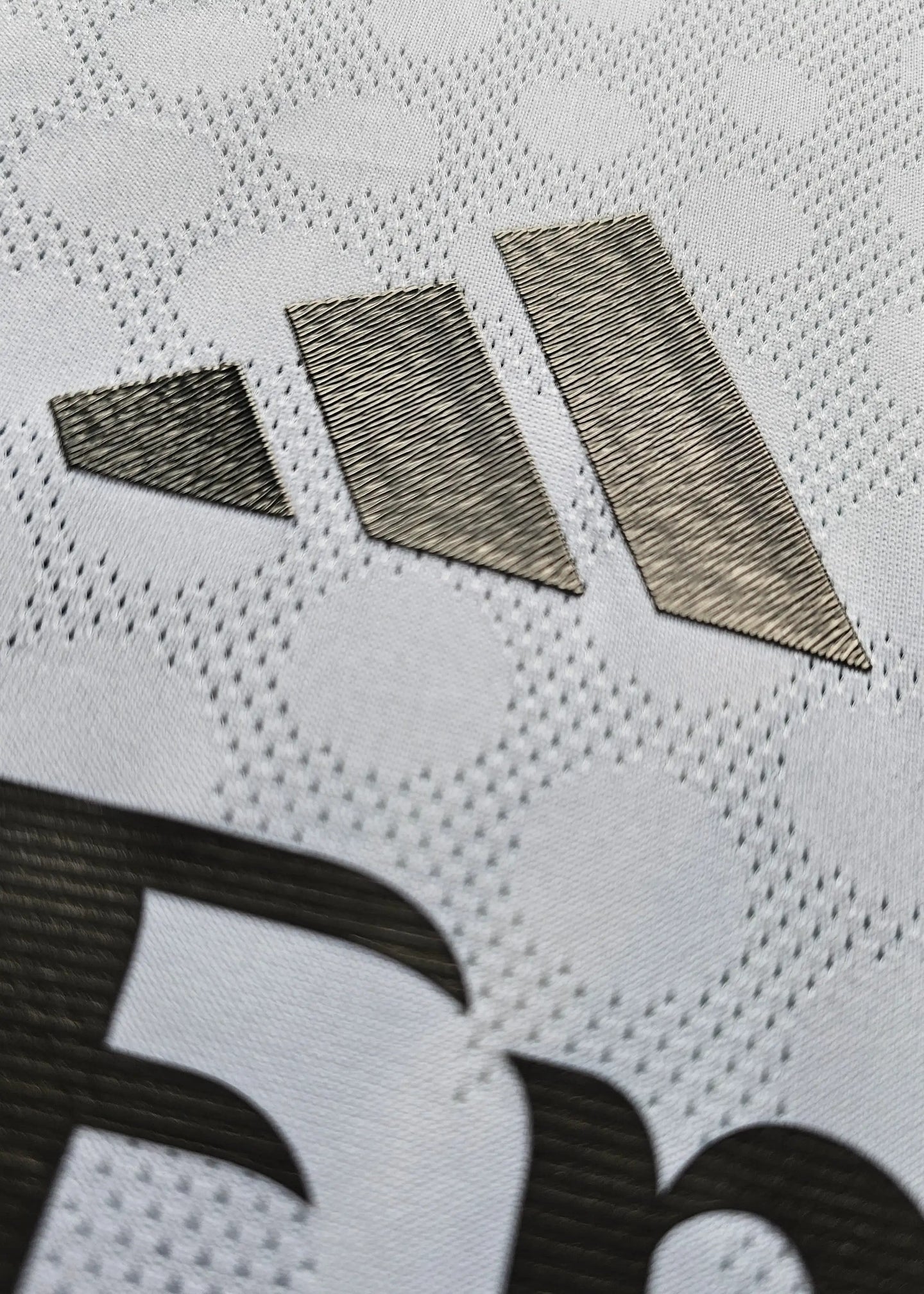 Close-up of the adidas logo detail on a white football shirt fabric.