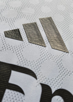 Close-up of the adidas logo detail on a white football shirt fabric.