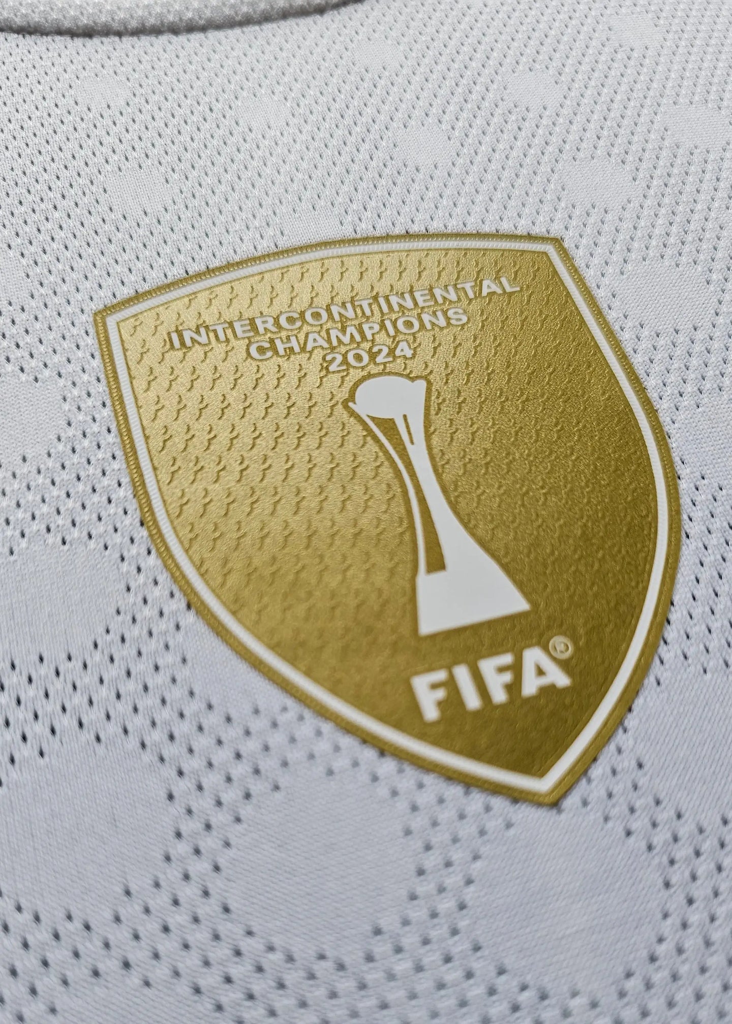 Close-up of the FIFA Intercontinental Champions 2024 badge in gold on white fabric.