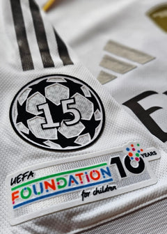 Close-up of UEFA badge with '15' and 'FOUNDATION 10 YEARS for children' text on white shirt.