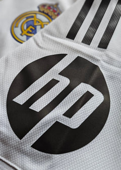 Close-up of Real Madrid crest and HP logo on white football shirt.
