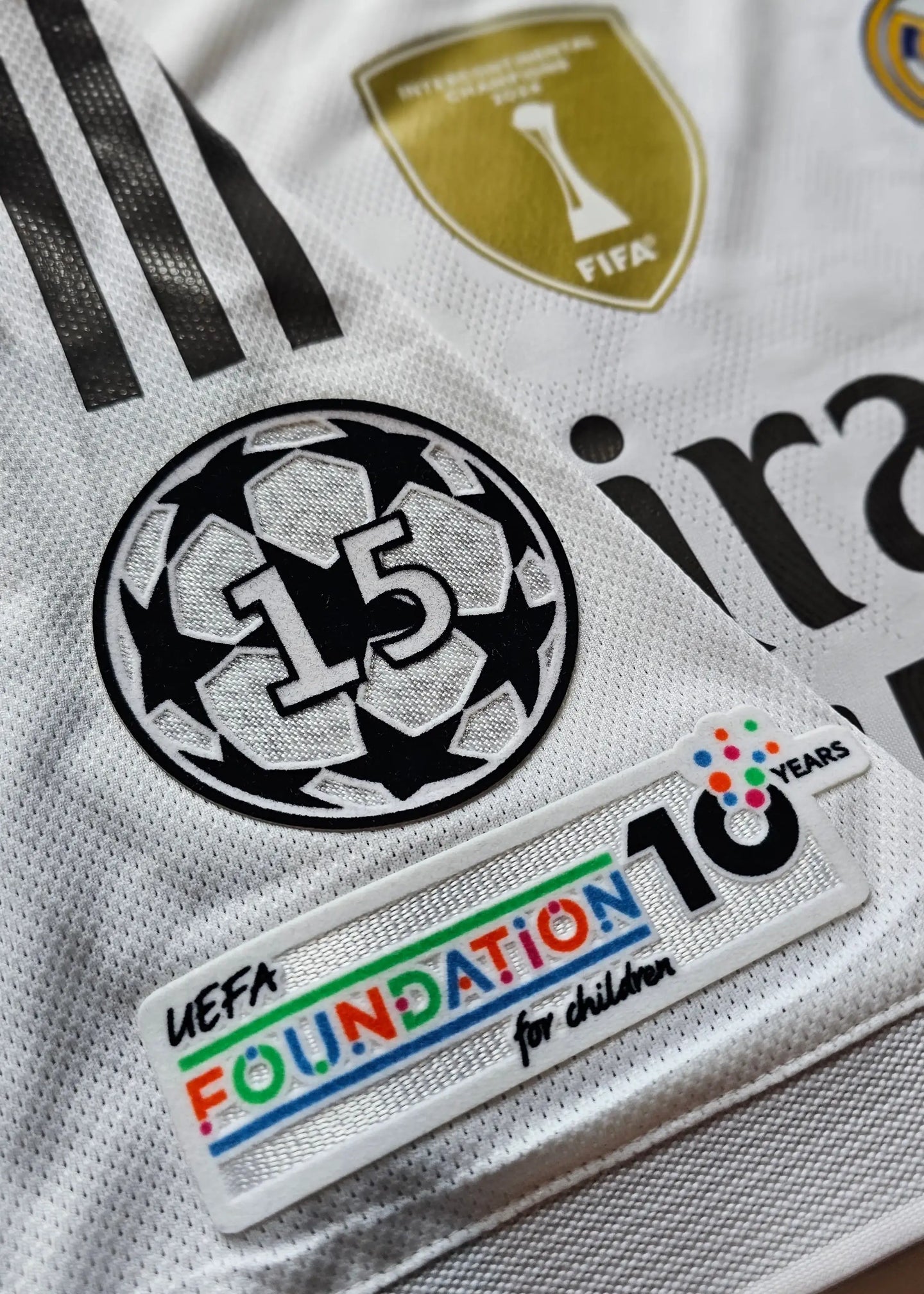 Detail view featuring UEFA Foundation badge and Champions League No. 15 emblem on a white football shirt.