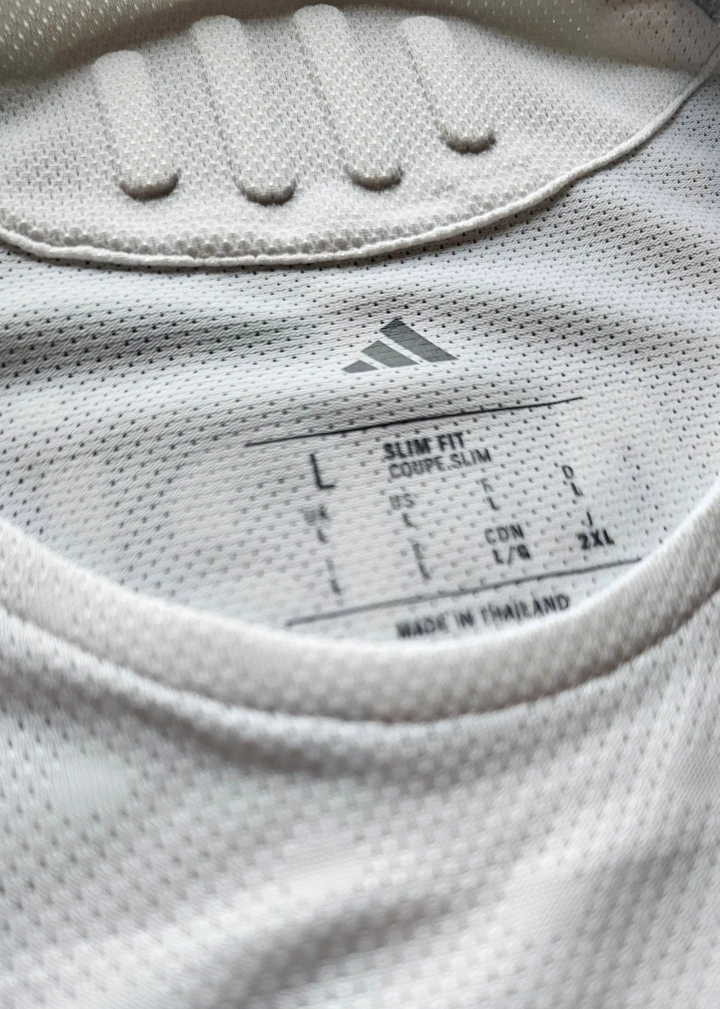 Close-up detail showing size label 'L' and 'Made in Thailand' on a white football shirt.