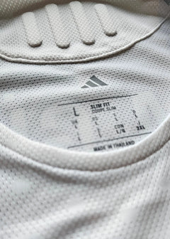 Close-up detail showing size label 'L' and 'Made in Thailand' on a white football shirt.
