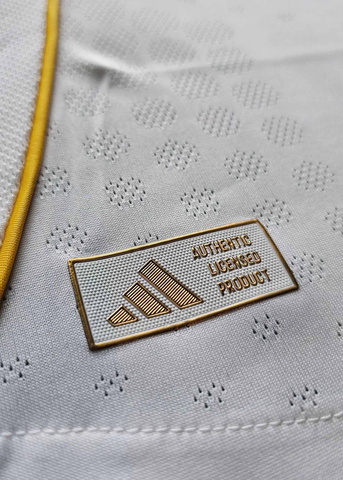 Close-up detail of the adidas logo and the text AUTHENTIC LICENSED PRODUCT on a white football shirt.