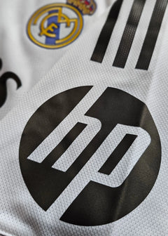 Close-up of the Real Madrid crest and HP sponsor logo on a white football shirt.