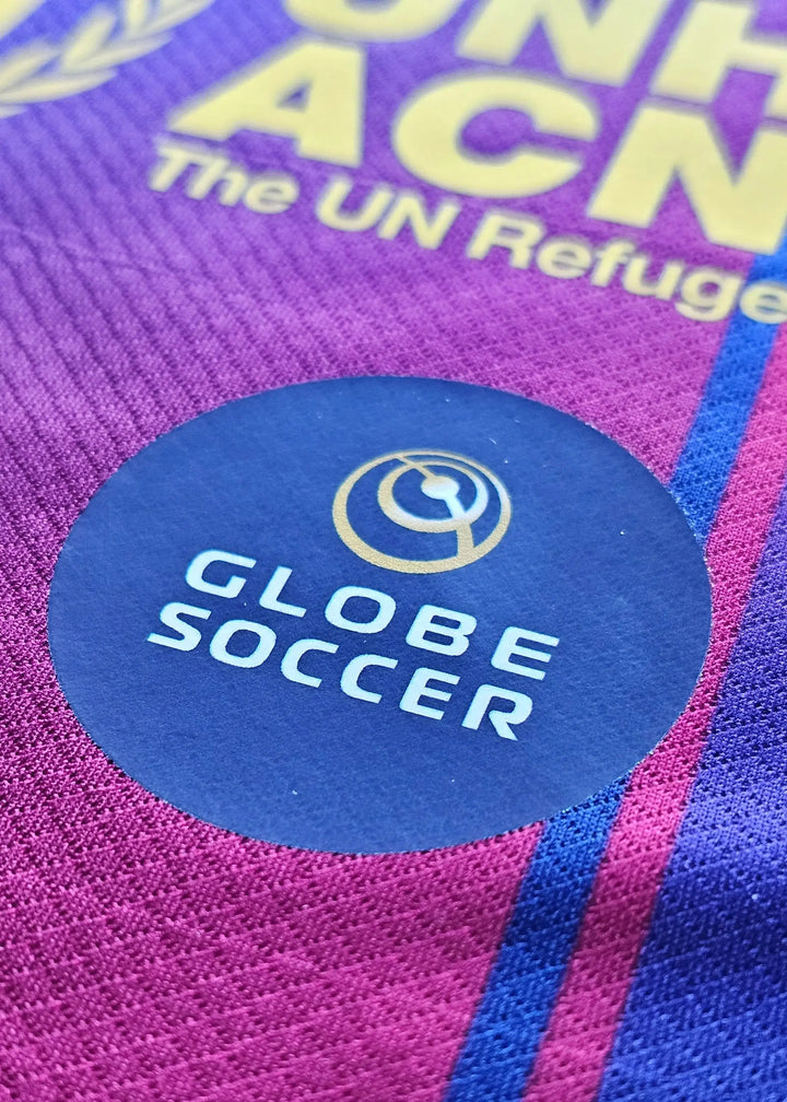 Crest detail showcasing the Globe Soccer logo on a purple and navy football shirt.