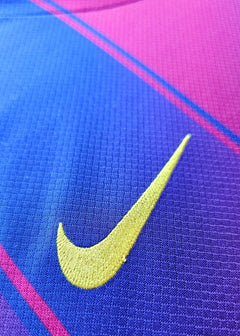 Close-up detail of the yellow Nike logo on a purple and pink football shirt.