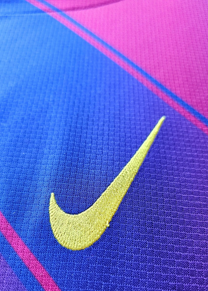 Close-up detail of the yellow Nike logo on a purple and pink football shirt.