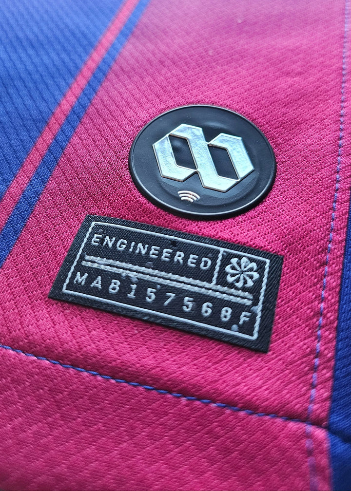 Close-up of engineered badge and care label on football shirt in navy, yellow, and purple.