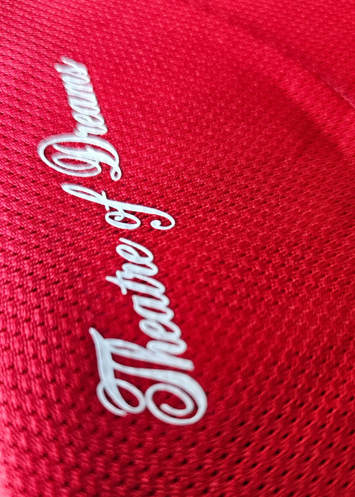 Close-up view of the embroidered 'Theatre of Dreams' in white on a red football shirt.
