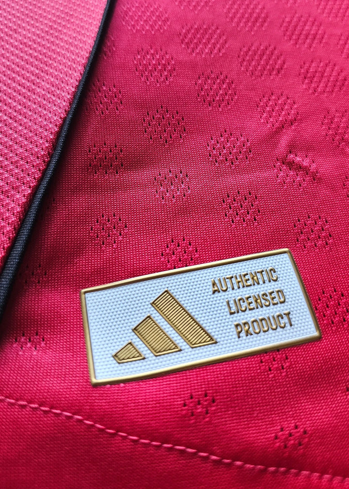 Close-up view of red fabric with ventilated patterns and adidas tag reading 'AUTHENTIC LICENSED PRODUCT'.
