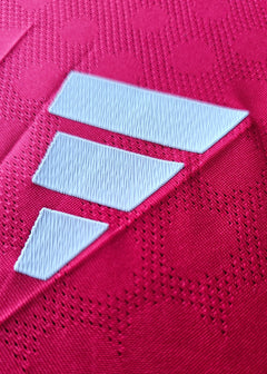 Close-up of red fabric featuring three white diagonal stripes on the football shirt.