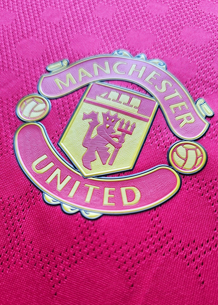 Close-up of the Manchester United crest on a red football shirt, with 'MANCHESTER' above 'UNITED'.