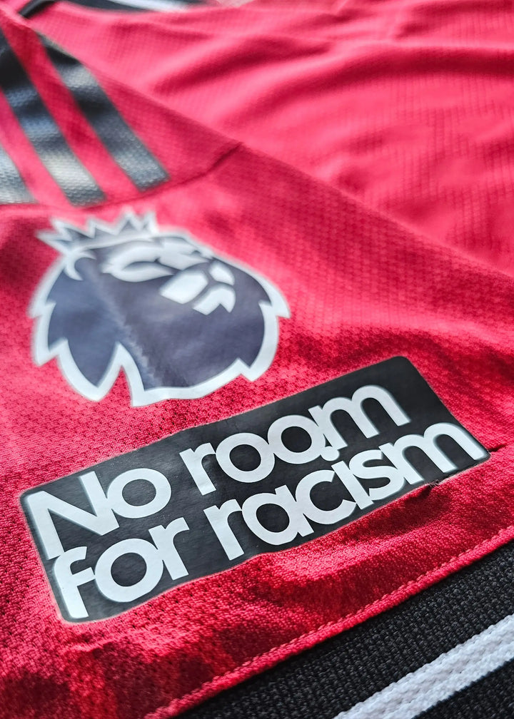 Close-up view of Manchester United crest and 'No room for racism' label on red football shirt.