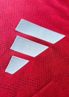 Close-up of the red fabric with three white adidas stripes and textured background.