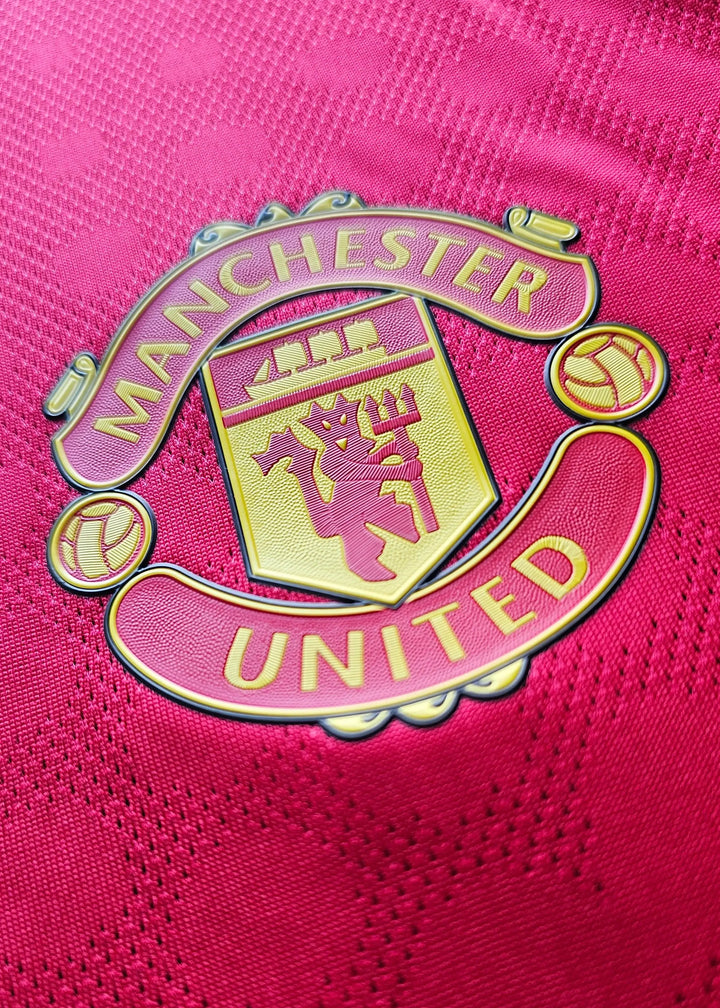 Detail of the Manchester United crest with gold trim on a red background.