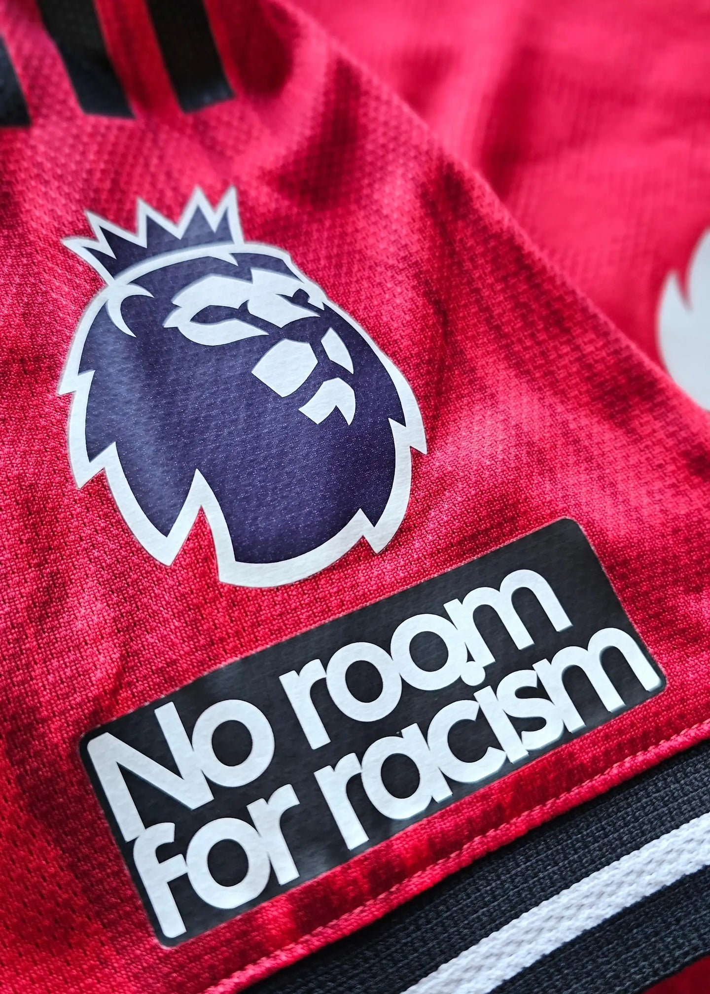 Close-up of the Premier League crest alongside the text 'No room for racism' on a red football shirt.