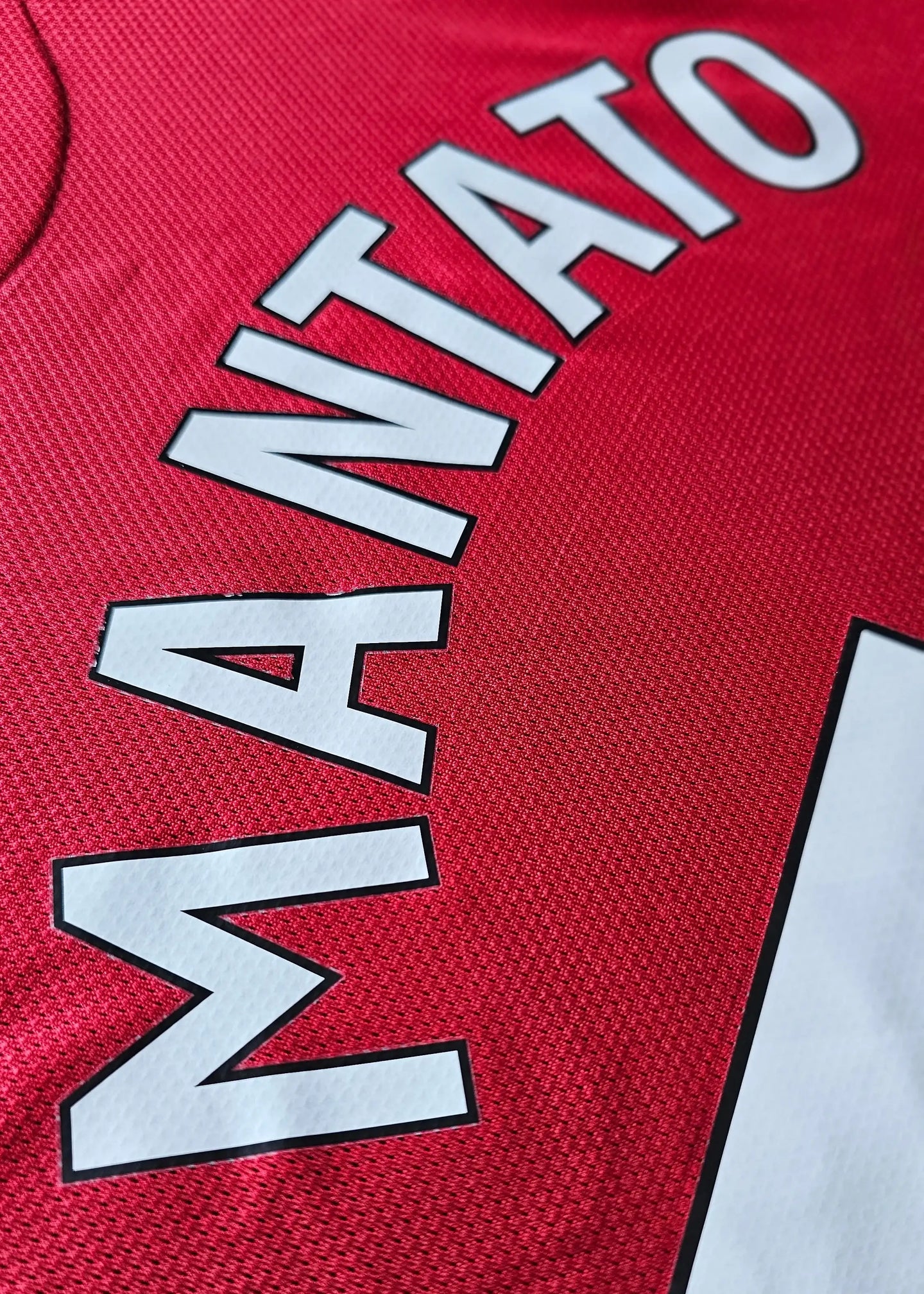 Close-up detail of the name 'MANTATO' in white lettering on a red football shirt.
