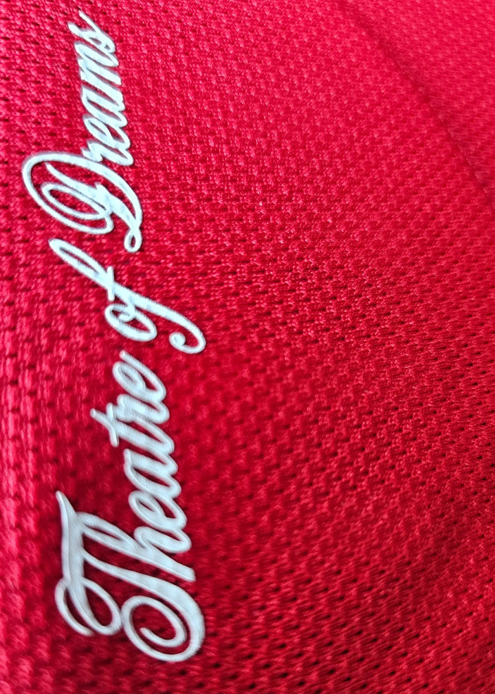 Close-up view of 'Theatre of Dreams' embroidered in white on red fabric.