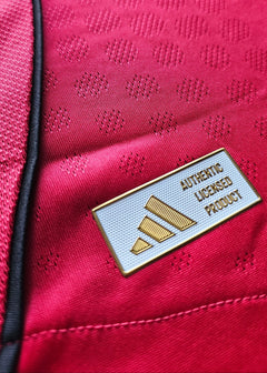 Close-up of adidas licensed product label on red fabric with textured patterns.