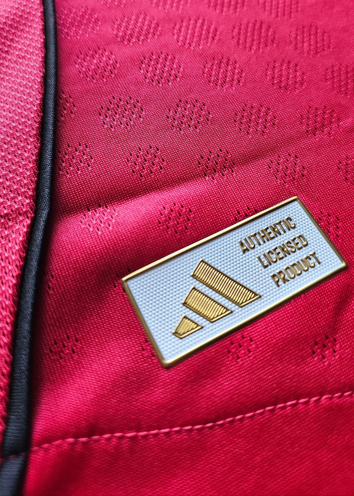 Close-up of adidas licensed product label on red fabric with textured patterns.