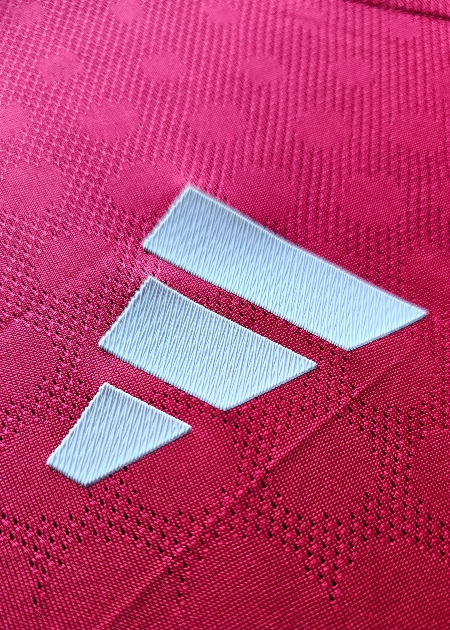 Close-up view of the adidas logo in white on a red football shirt.